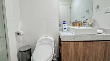 Un baño moderno con inodoro blanco, un bote de basura, lavamanos de mármol y tocador de madera.