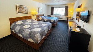 Ein Hotelzimmer mit zwei Betten, einem Schreibtisch, einem Fernseher und einem Fenster mit Vorhängen.