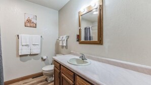 Un baño con tocador de madera, lavamanos, inodoro y espejo con iluminación.