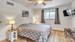 Un dormitorio con cama, ventilador de techo, televisor, escritorio y una silla.