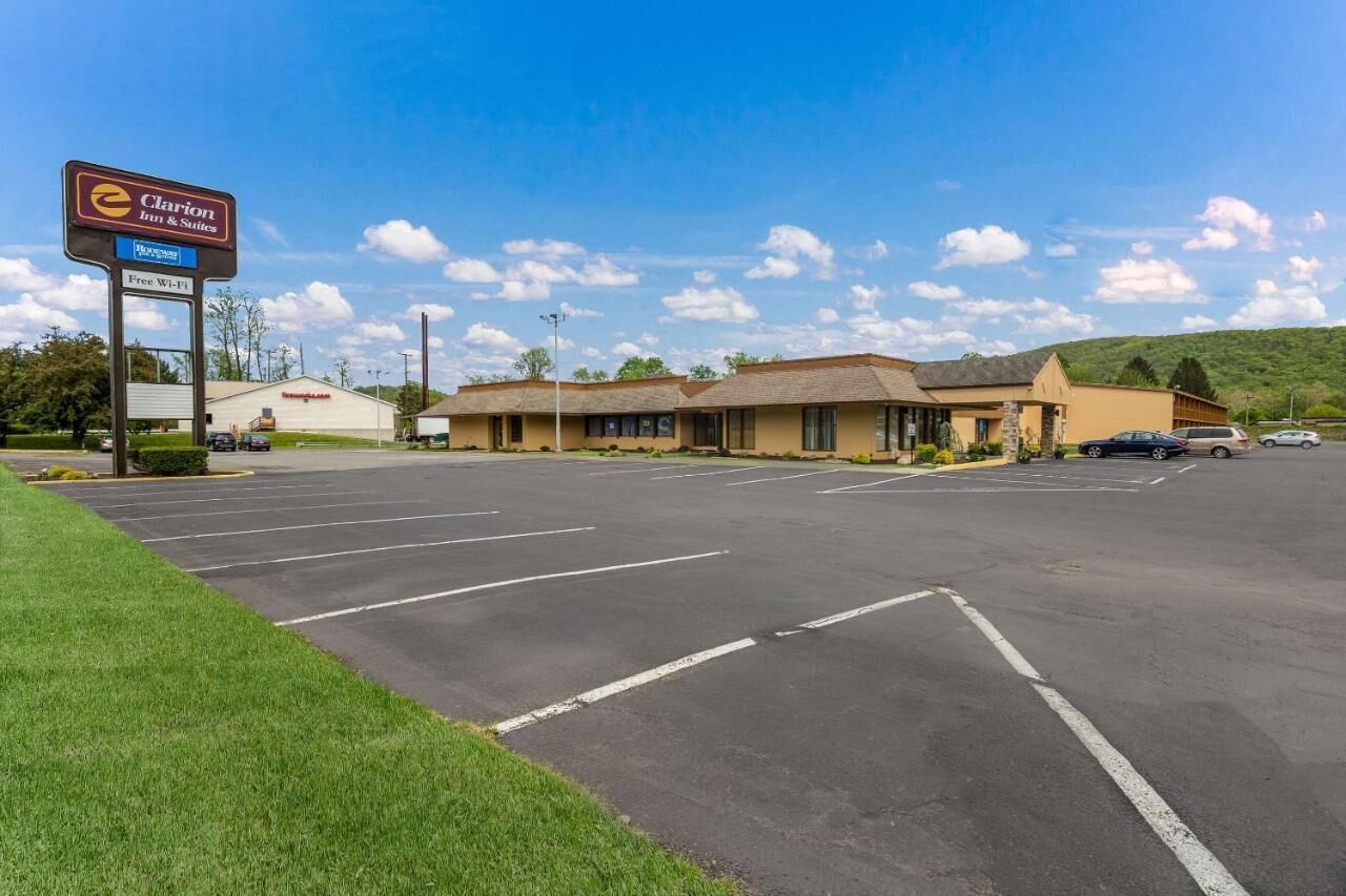 A Clarion Inn & Suites with a large parking lot and a building with a flat roof and beige exterior.