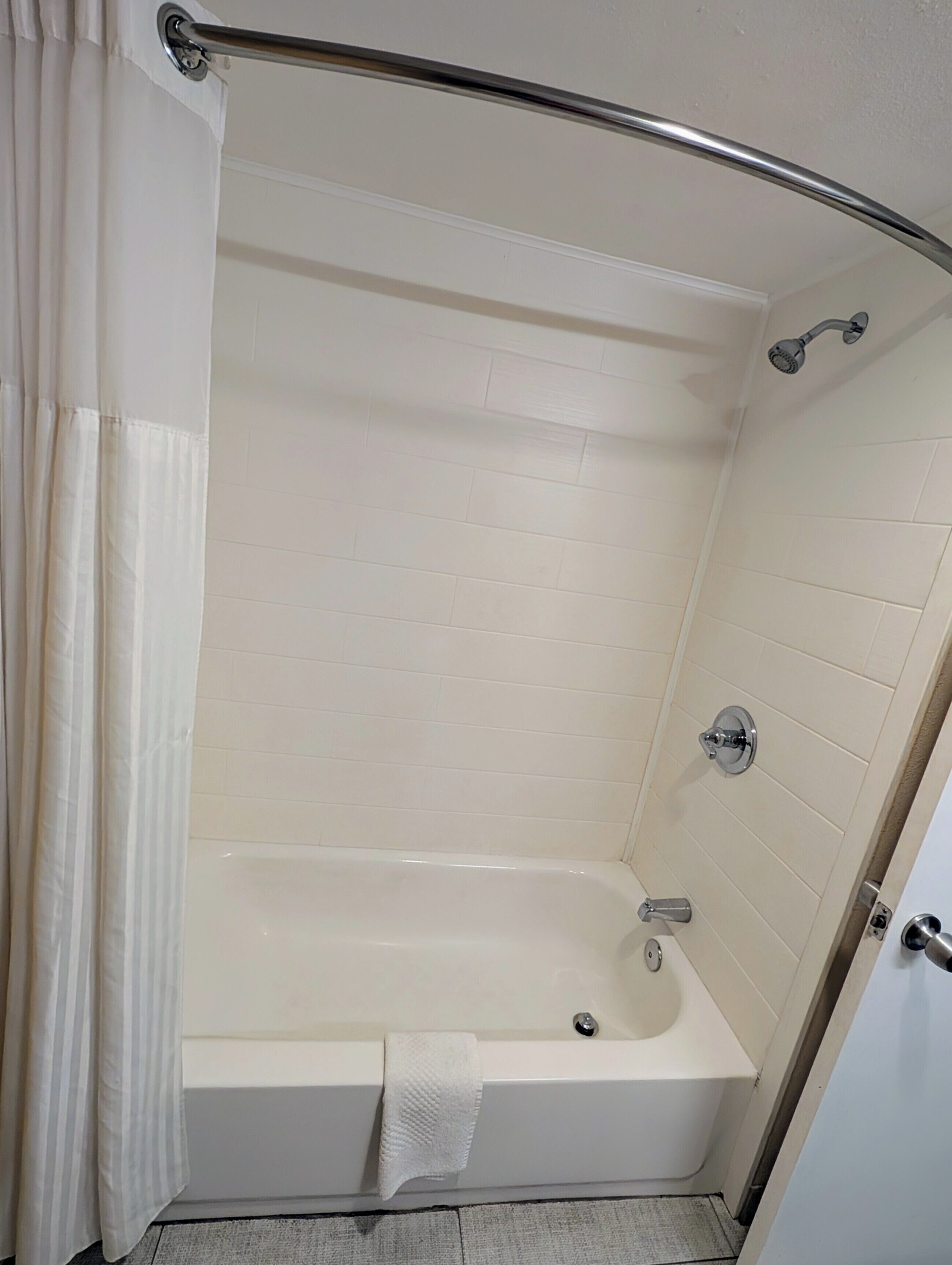A walk-in shower with a glass door, white tiled walls, and a white bathtub.