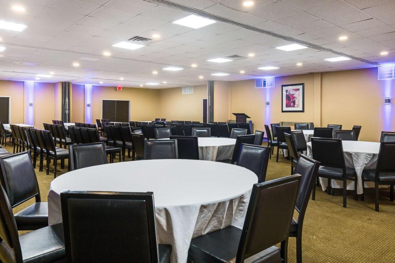 Un salón de conferencias con varias mesas redondas y sillas, equipado con un atril y una pantalla para proyector.