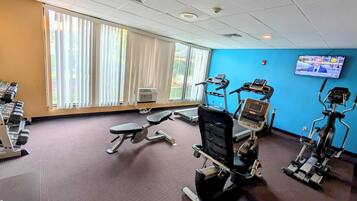 Een sportschool met trainingsapparatuur, grote ramen en een televisiescherm.