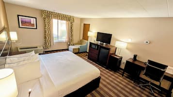 Ein Hotelzimmer mit Bett, Schreibtisch, Stuhl, Fernseher und einem Fenster mit Vorhängen.