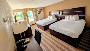 Een hotelkamer met twee bedden, een bureau met lamp, een telefoon en een raam met gordijnen.