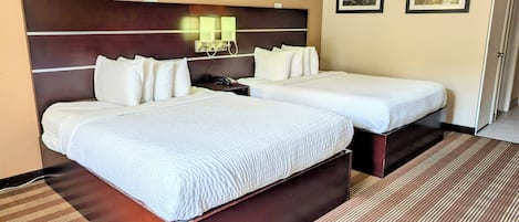 A hotel room with two beds, a headboard, a nightstand, a telephone, and two framed pictures on the wall.
