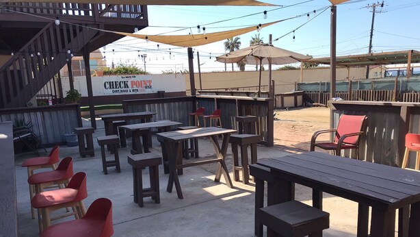 Een buitengebied met een terras, houten tafels en rode stoelen, een overdekt zitgedeelte en een bordje met 'CHECK POINT Dirt Bikes & Mtn. Club'.
