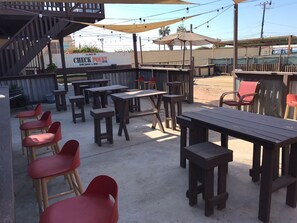 Een buitengebied met een terras, houten tafels en rode stoelen, een overdekt zitgedeelte en een bordje met 'CHECK POINT Dirt Bikes & Mtn. Club'.