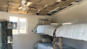 Een kamer met stapelbedden, een plafondventilator, een raam en een opbergruimte.