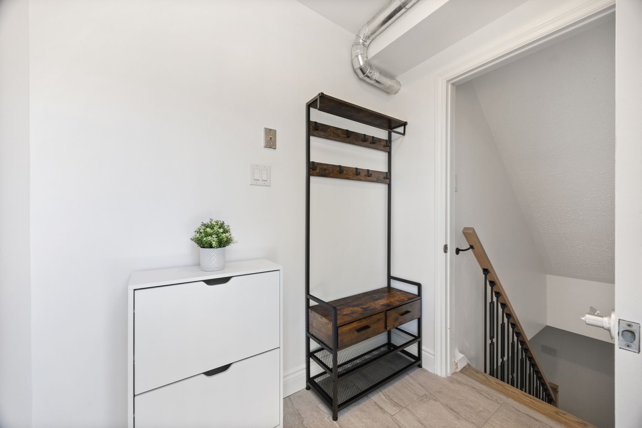 A staircase with a wooden handrail and a white wall with a white cabinet and a plant.