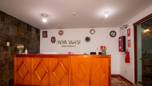 A reception desk with a stone wall backdrop, a sign reading "INYA WASI APARTMENTS", and a patterned floor. - Inyawasi Aparthotel (Cusco)
