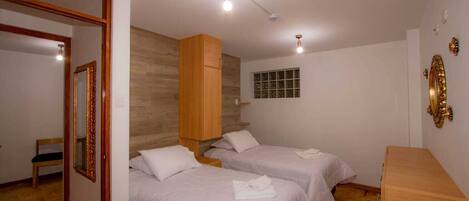 A hotel room with two beds, a wooden wardrobe, a mirror, and a small window.