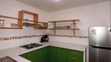A kitchen with green cabinets, a stainless steel refrigerator, and wooden shelves above the counter.