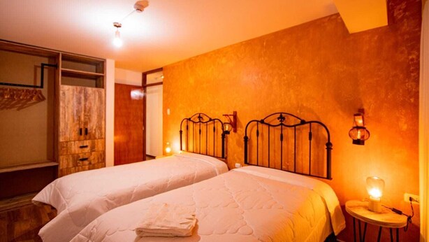 A hotel room with two beds, a wooden wardrobe, and a mirror. - Inyawasi Aparthotel (Cusco)