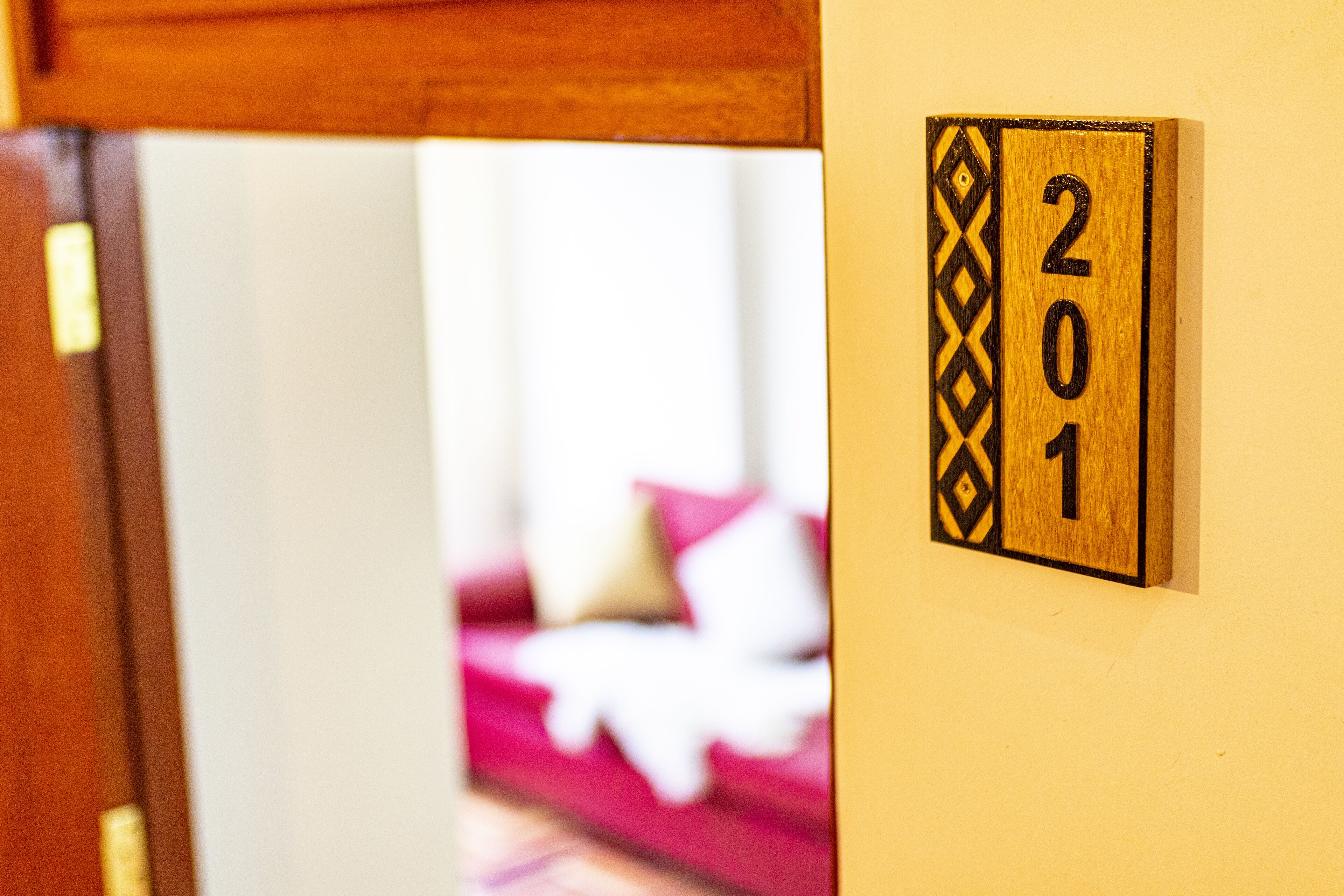 A door frame with a wooden door partially open, revealing a room with a red couch and a wall-mounted number plate displaying "201".