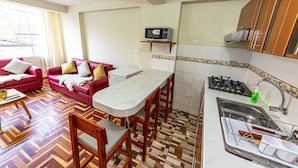 A compact living space with a kitchenette, a dining area with a table and chairs, a red sofa, and a patterned floor. - Inyawasi Aparthotel (Cusco)