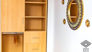 A wooden wardrobe with multiple shelves and drawers, a mirror with ornate gold and blue decorations, and a logo for Inya Wasi Apartment Hotel. - Inyawasi Aparthotel (Cusco)