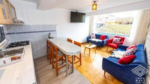 A modern apartment with a kitchen, dining area, and living room. It includes a TV, a balcony with a view of a stadium, and a sofa set. - Inyawasi Aparthotel (Cusco)