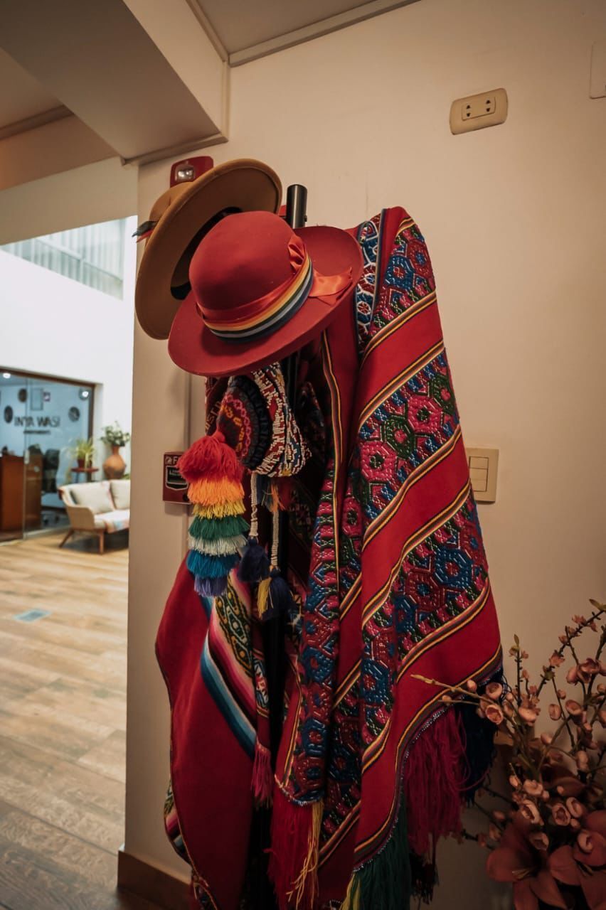 A room with a red patterned blanket draped over a chair, a red hat on the wall, and a view of a building outside.