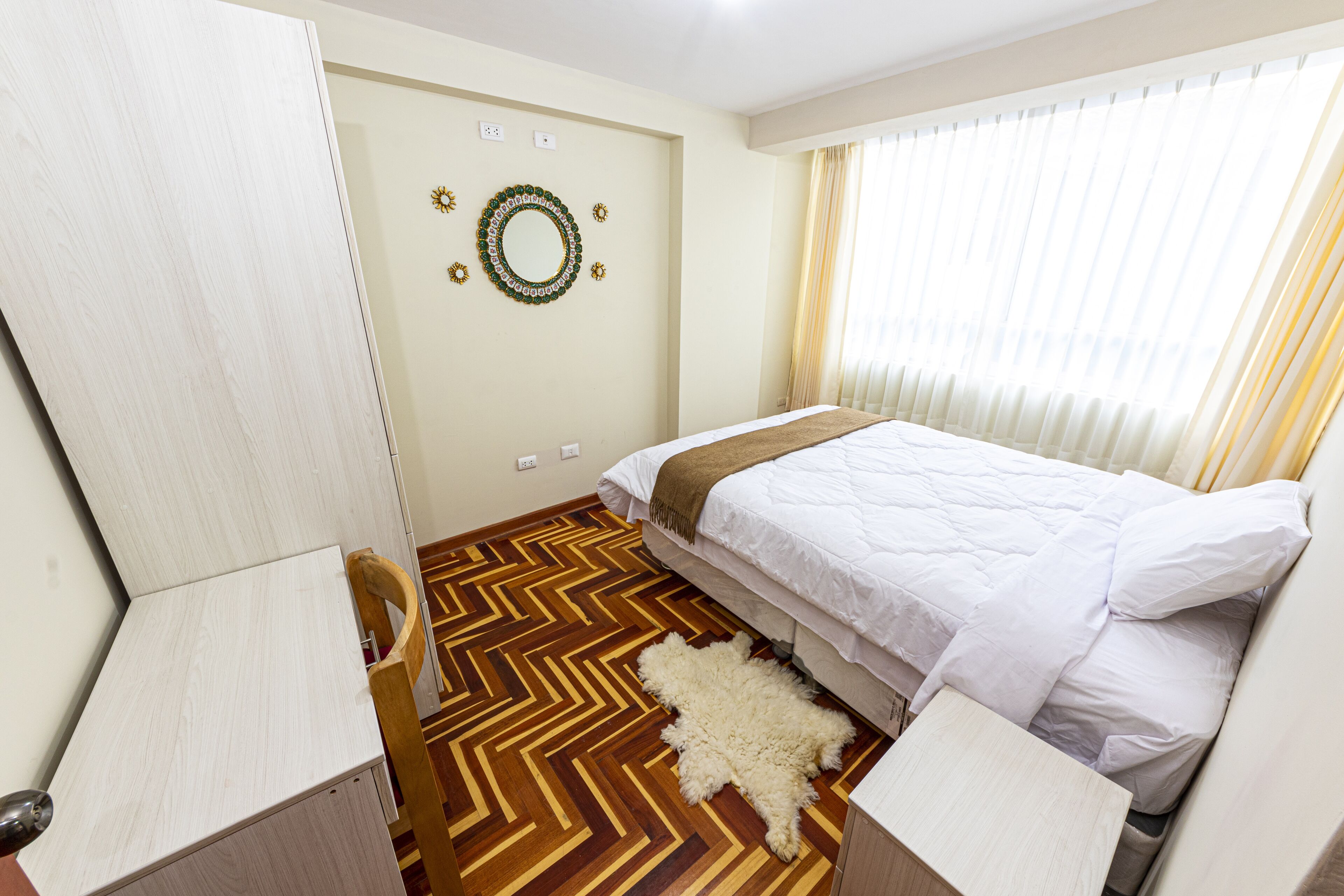 A room with a bed, a wooden floor, a rug, and a wall decoration.
