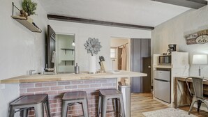 A modern kitchen with a brick backsplash, a wooden countertop, and three metal bar stools. - Quest Rest - Unit 6 (Colorado Springs)