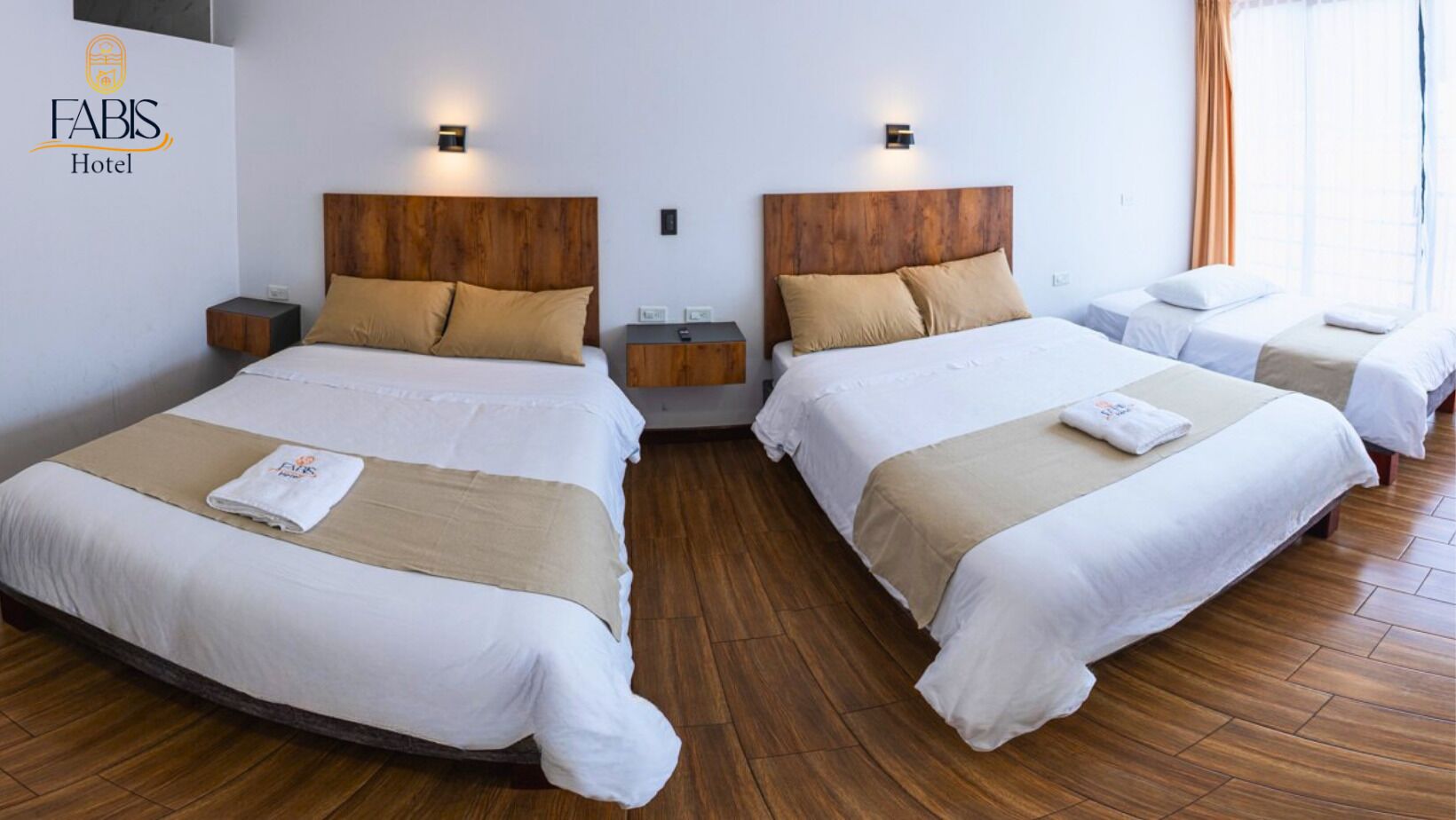 A hotel room with two beds, wooden headboards, bedside tables, and a nightstand.