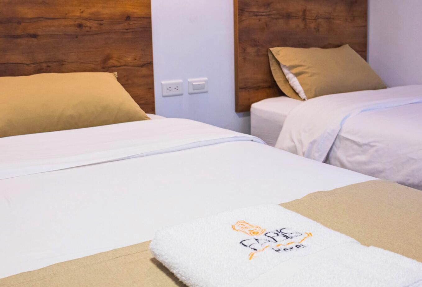 A hotel room with two beds, each with white bedding and beige pillows. There is a logo for FABIS Hotel on the left side of the image.