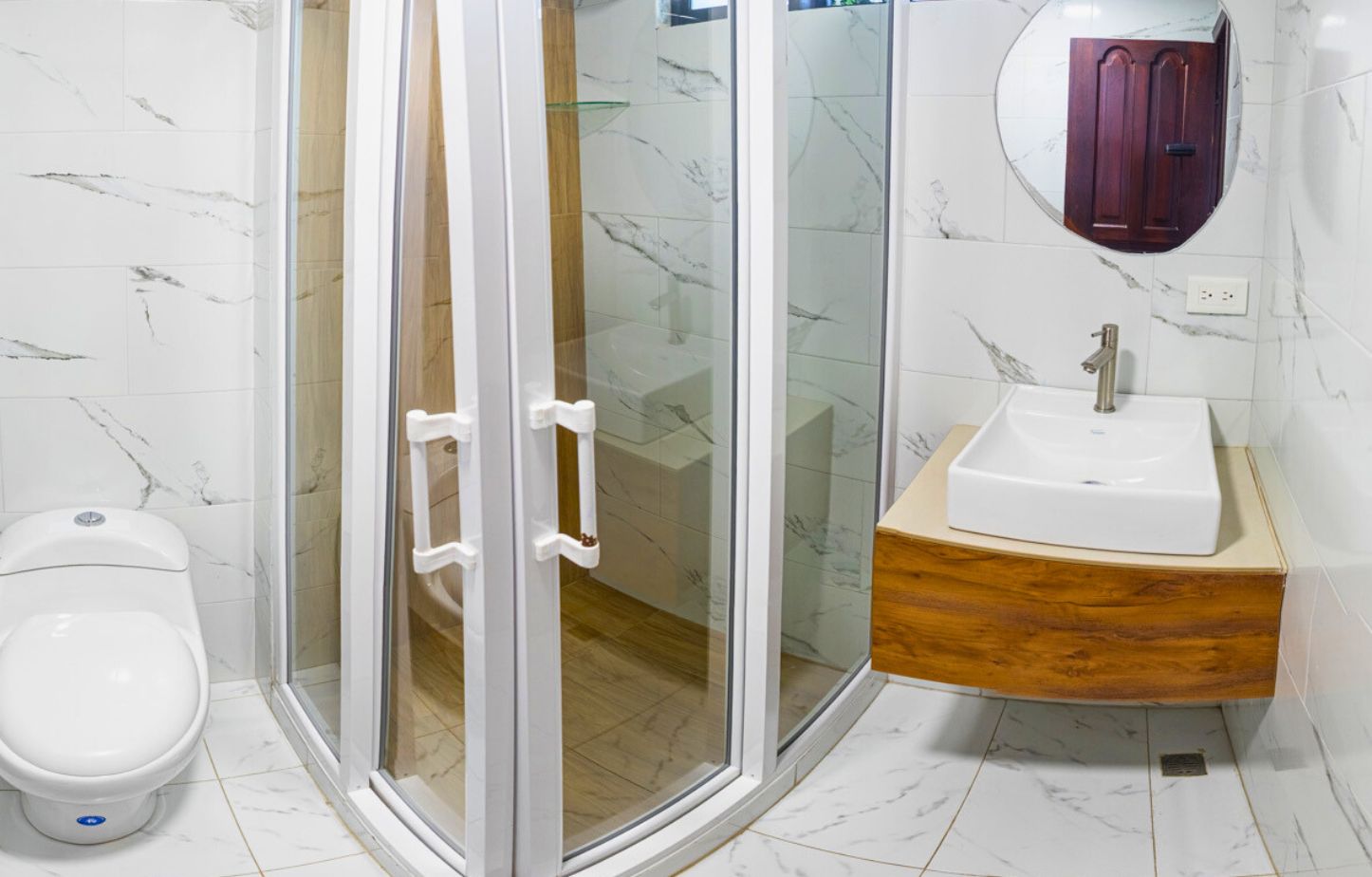 Un baño con inodoro, ducha con mampara de vidrio y lavamanos con encimera de madera.