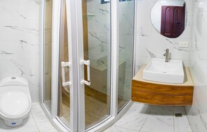 A bathroom with a toilet, a glass-enclosed shower, and a sink with a wooden countertop. - FABIS HOTEL (Baños de Agua Santa)