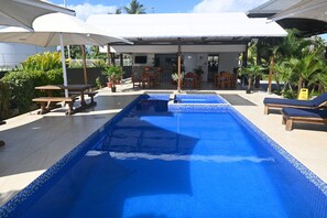A swimming pool with lounge chairs and umbrellas, surrounded by potted plants and a bar area. - New Door Apartments (Nadi)