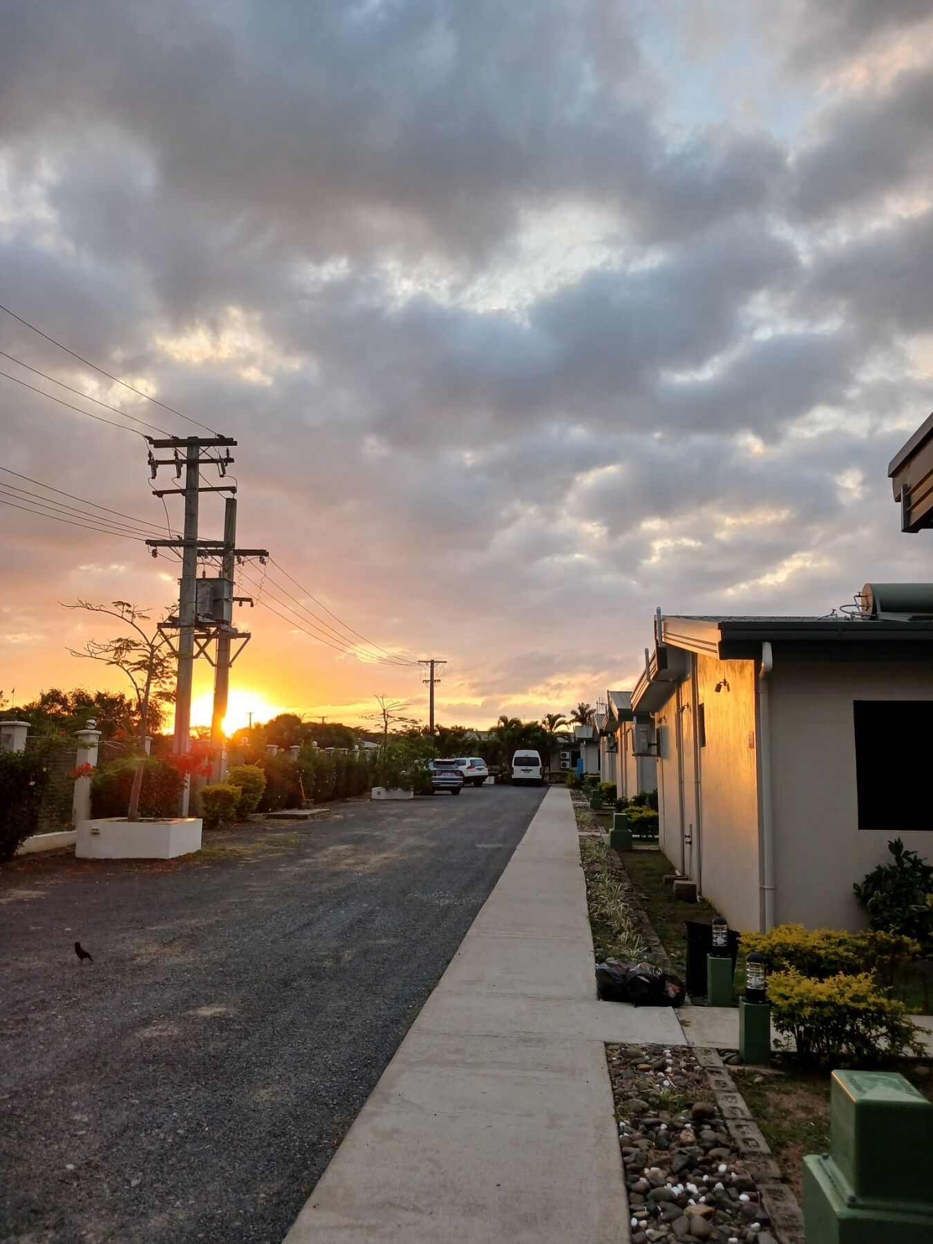 Eine Wohnstraße bei Sonnenuntergang mit Häusern an beiden Seiten, wolkenlosem Himmel und einem geparkten Rettungswagen.