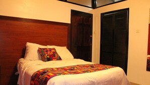 A neatly made bed with a colorful quilt and pillows, a wooden headboard, and a door with a black frame.