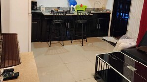 A compact kitchen with a clock, bar stools, and a refrigerator.