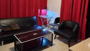 A living room with a black sofa, a glass coffee table, a black armchair, and red curtains.