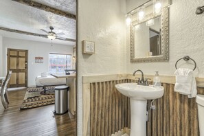 Ein Badezimmer mit einer Wand in Holzoptik, einem weißen Waschbecken und einem beleuchteten Spiegel.