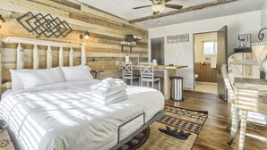 A spacious bedroom with a large bed, wooden walls, a ceiling fan, and a desk area with a chair and a coffee machine.