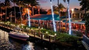 A waterfront restaurant with outdoor seating, palm trees, and a dock with a boat. - HOLIDAY RETREAT.★★★★★ 12. NEAR BEACHES / PGA / DOWNTOWN / ROGER DEAN STADIUM (Palm Beach Gardens)