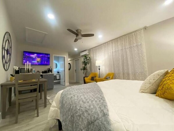 A hotel room with a large bed, a desk with a chair, a TV, and a ceiling fan.