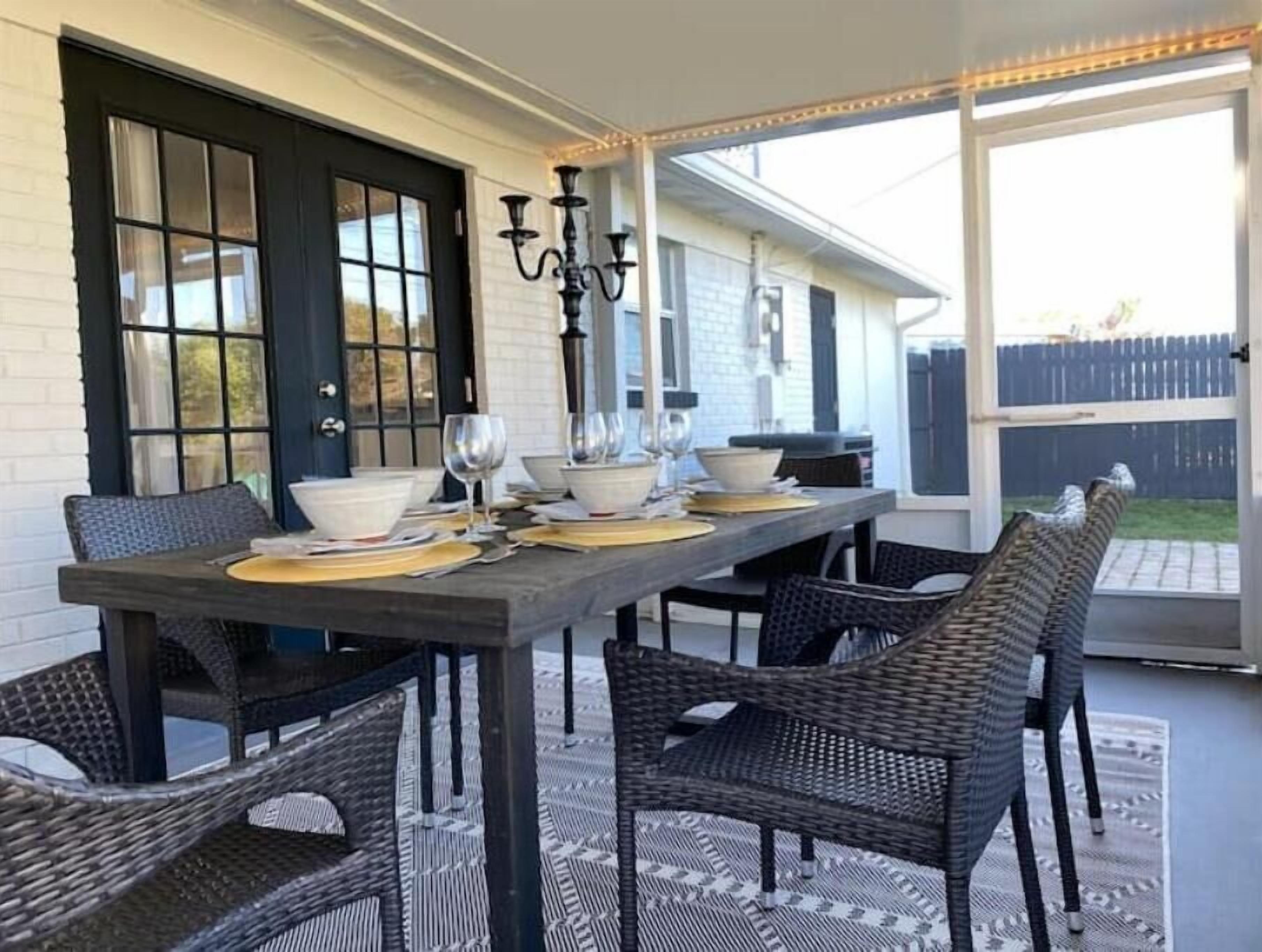 Un espace de restauration en plein air avec une longue table, des chaises en osier et un chandelier noir.