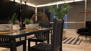 Un comedor con una mesa de madera oscura dispuesta para dos personas, rodeado de sillas de mimbre y una silla colgante.