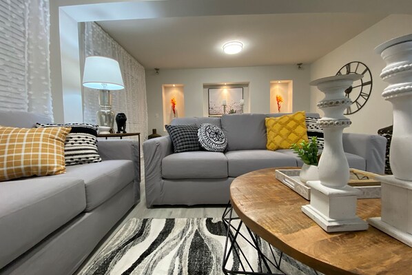 A modern living room with a grey sofa, patterned cushions, a wooden coffee table, and decorative items. - GULL RETREAT.★★★★★ 10. NEAR BEACHES / PGA / DOWNTOWN / ROGER DEAN STADIUM (Palm Beach Gardens)