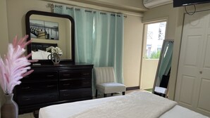 A bedroom with a bed, dresser, chair, mirror, and a window with curtains.