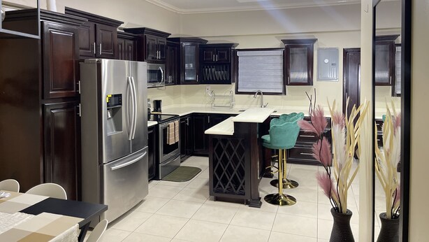 A modern kitchen with dark cabinetry, stainless steel appliances, a bar stool, and a decorative vase.