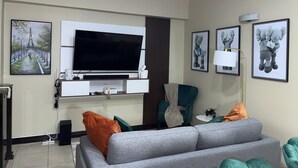 A living room with a flat-screen TV, a sofa, a chair, and artwork on the walls.