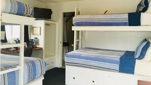 Une chambre de dortoir avec des lits superposés, un bureau avec une chaise, une télévision et une porte donnant sur une autre pièce.