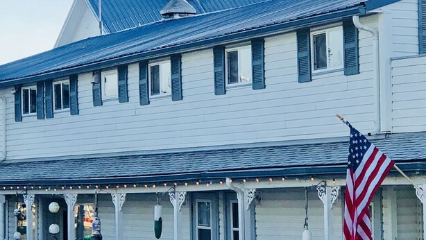 Un bâtiment blanc avec un toit bleu, une véranda décorée de guirlandes lumineuses et un drapeau américain.