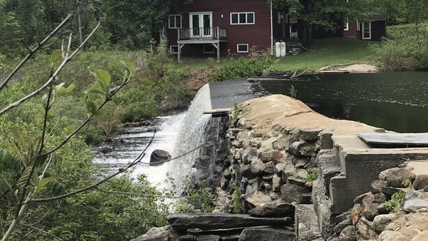 A house with a stone staircase leading to a dock over a small waterfall. - Farmhouse on Otis Pond (Otis)
