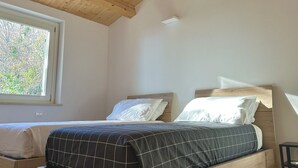 Une chambre avec deux lits, des têtes de lit en bois, une grande fenêtre et un appareil de climatisation.