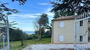 Un bâtiment de couleur beige, avec un toit en tuiles, une allée gravillonnée et un portail blanc.